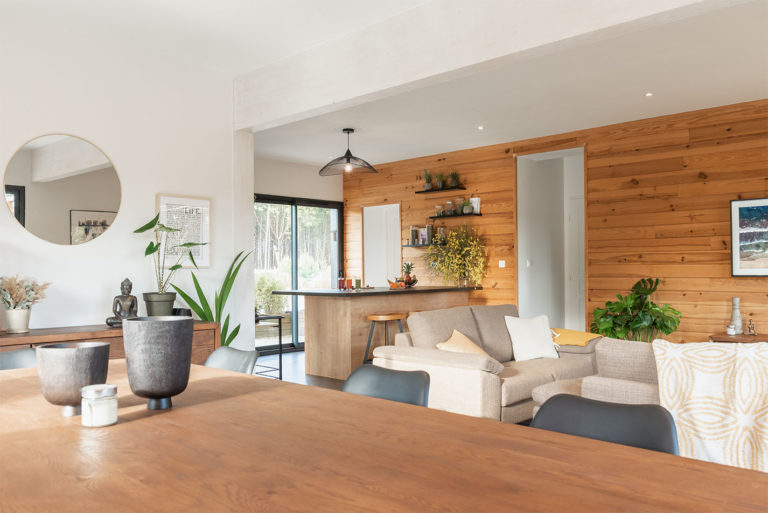 Photo d'un intÃ©rieur de maison chaleureux en bois et blanc donnant sur un salon et espace cuisine avec plan bar.