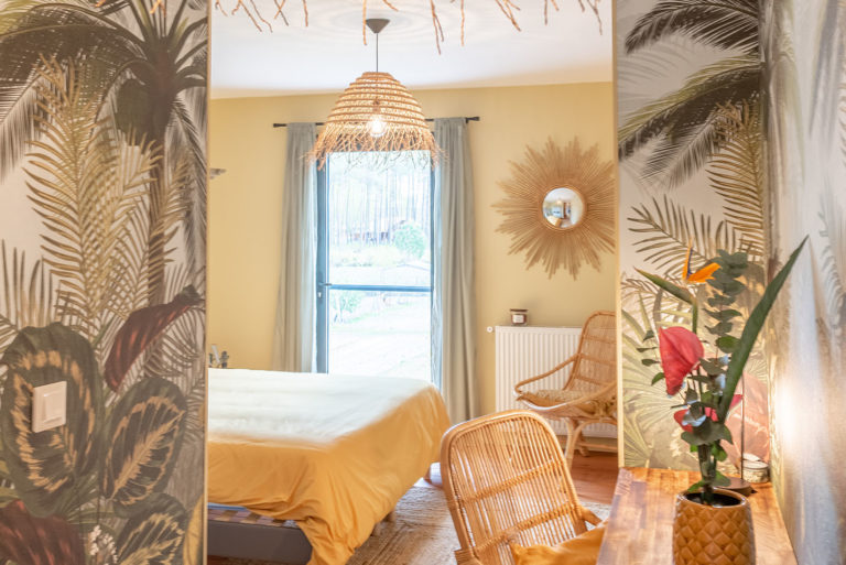 Photo d'une chambre avec tapisserie végétale et pot de fleur avec fleur tropicales ainsi qu'un lustre en paille.