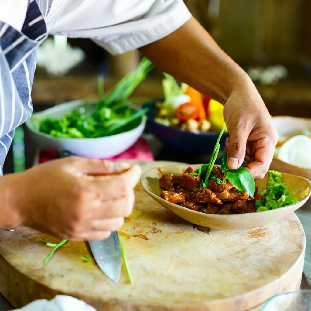 Photo d'une personne dont on voit les 2 mains en train de cuisiner et placer une belle feuille de basilic sur une assiette colorée.