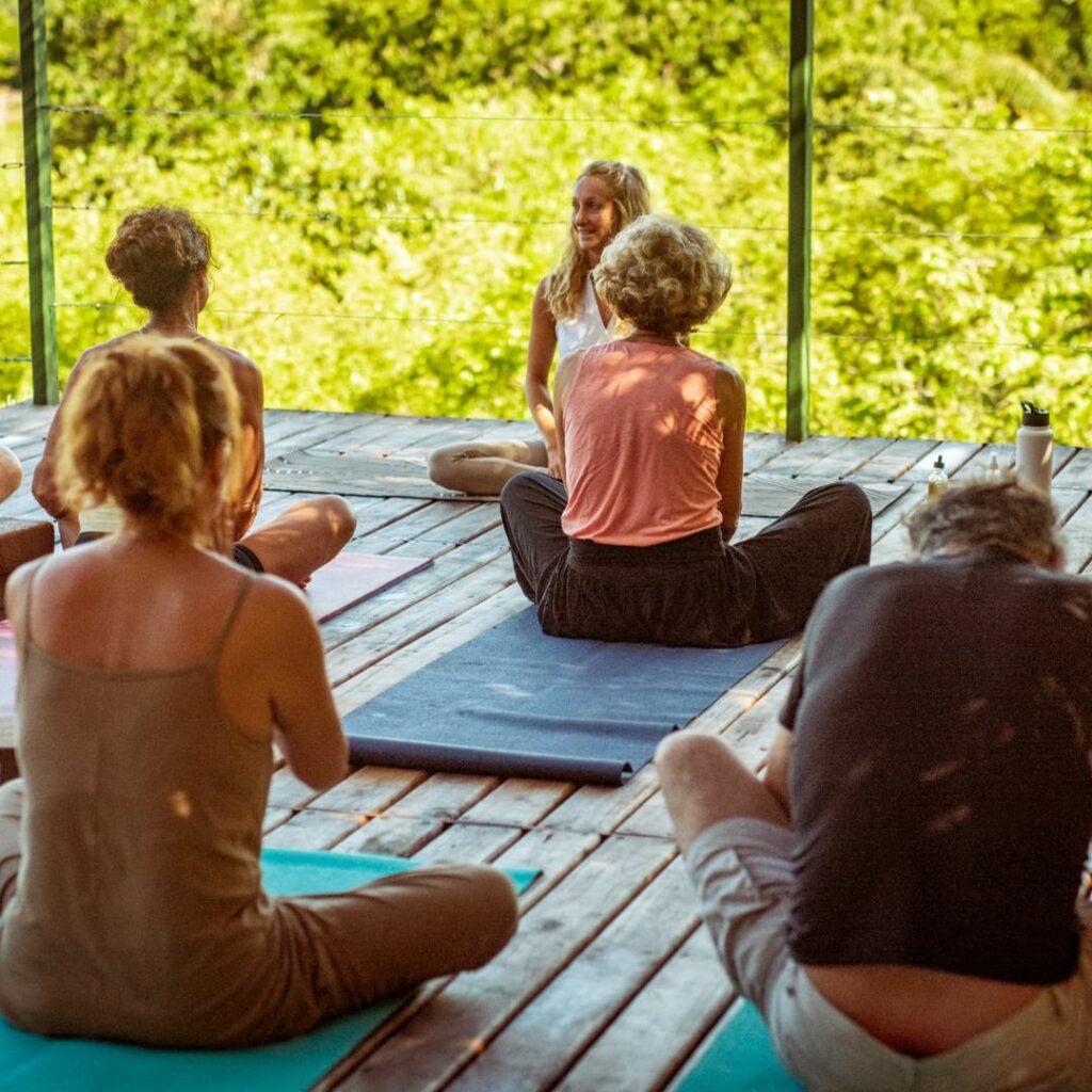 Photo d'un groupe de personne en posture de yoga au sol sur une terrasse en bois.