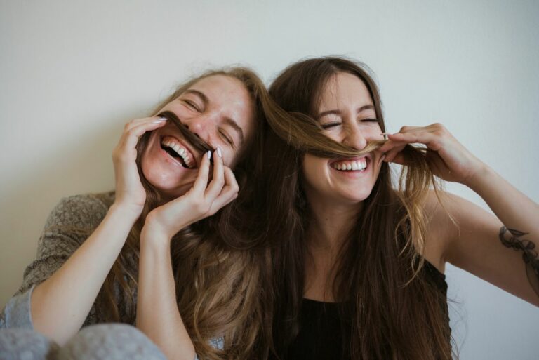 Photos de deux jeunes femmes souriantes et s'amusant avec leurs cheveux pour faire des moustaches.