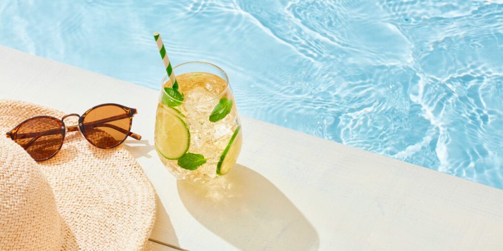 Photo d'un bord de piscine avec une paire de lunette de soleil et un verre de citronnade avec une paille.