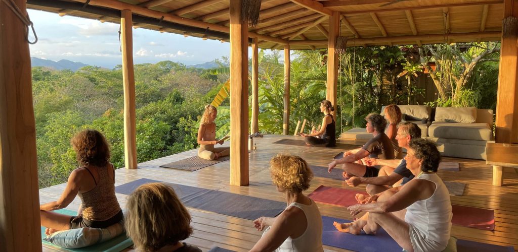 Photo d'un groupe assistant à un cours de yoga sur une terrasse en bois devant une vue de jungle.