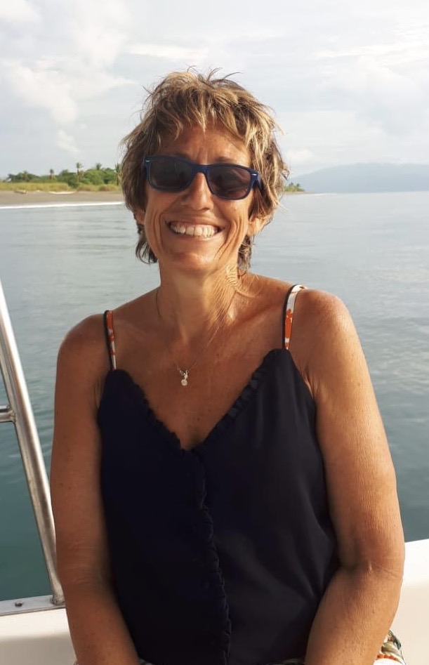 Photo d'une femme souriante avec des lunettes devant l'océan.