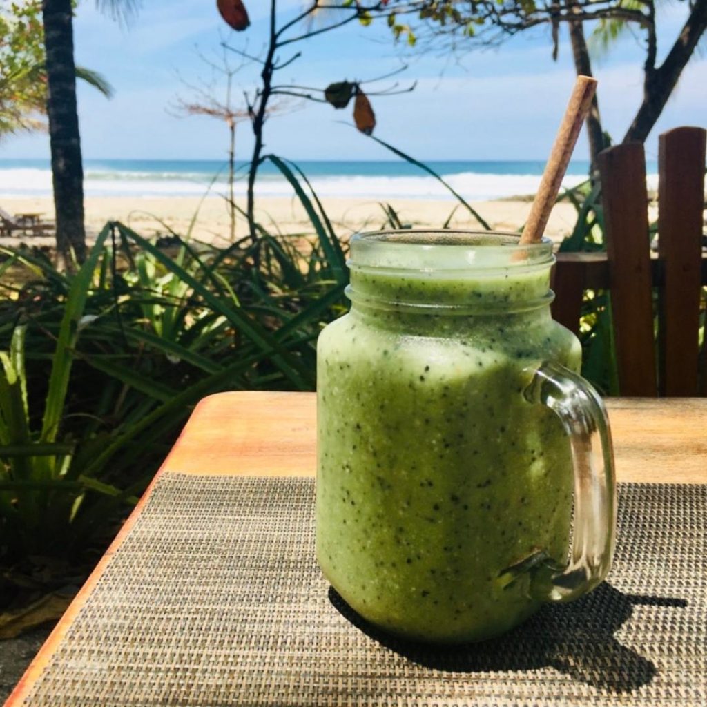 Photo d'un beau smoothie vert avec une paille posée sur une table devant la plage.