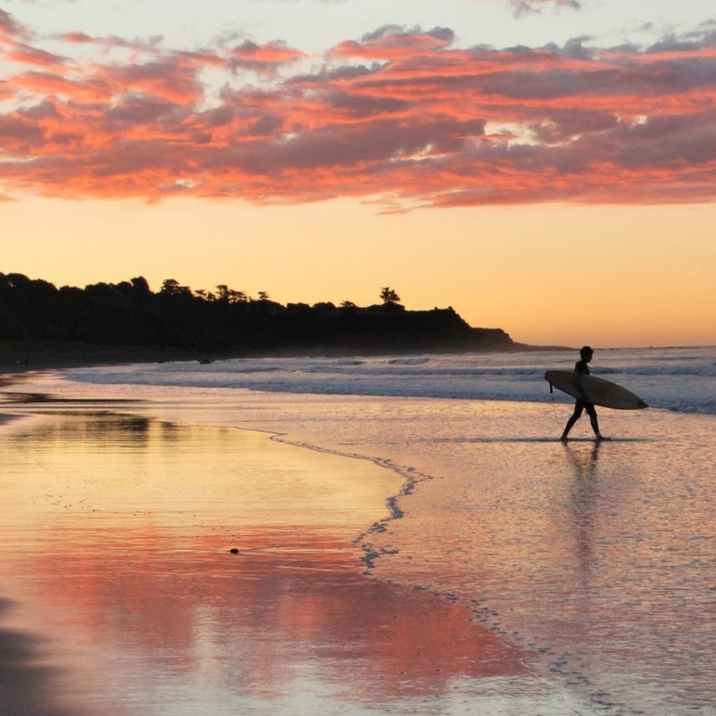 Photo d'une personne avec sa planche de surf au coucher du soleil.