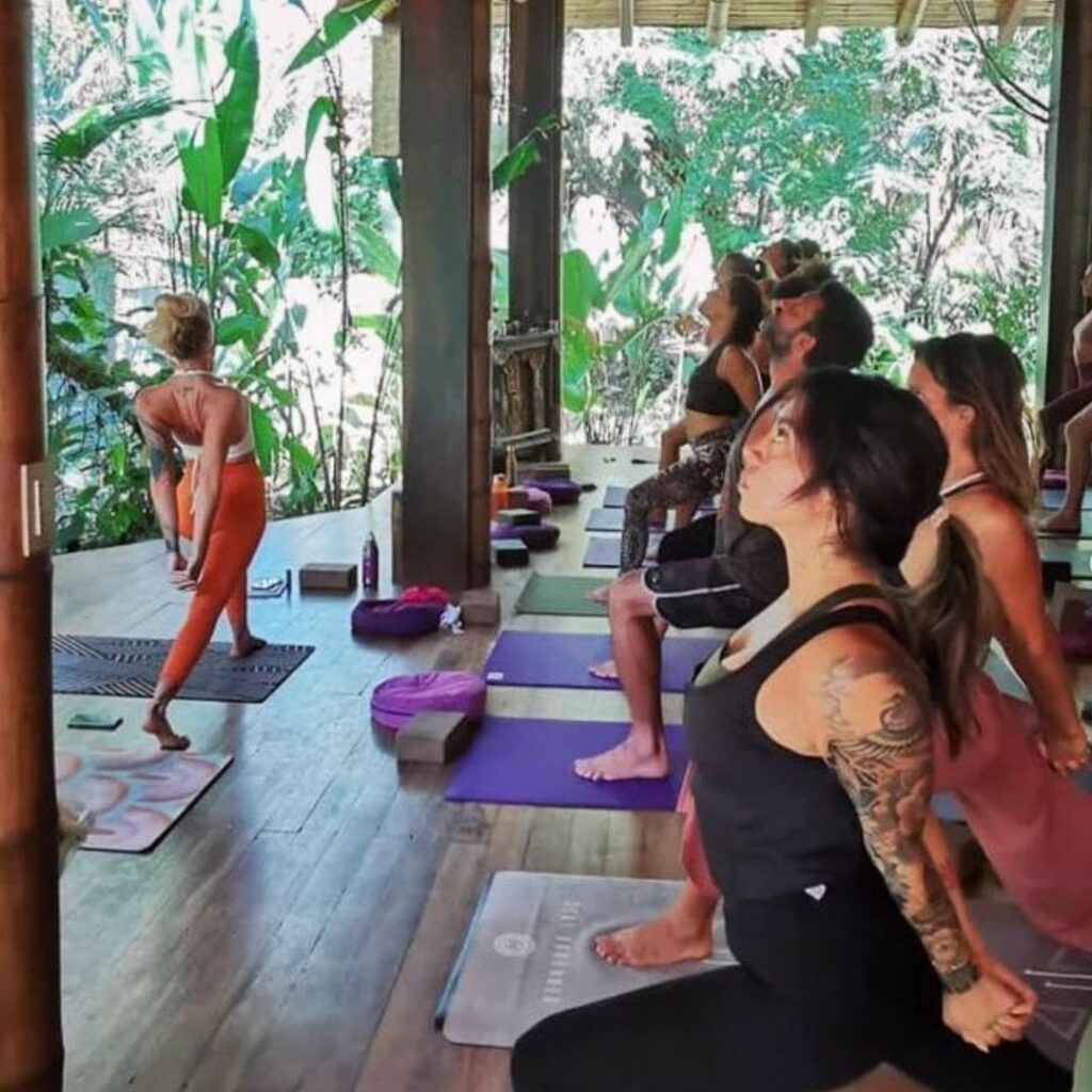 Photo d'Amelina animant un cours de yoga devant un groupe. Ils sont tous sur une terrasse en bois avec fond de végétation tropicale au Costa Rica.