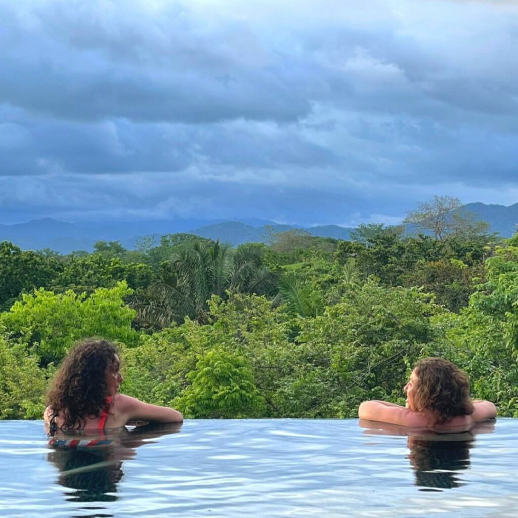 Photo de 2 femmes dans une piscine à débordement avec vue sur la nature et ciel orageux.