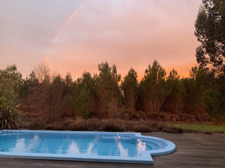Photo d'une piscine avec vue sur les landes et un ocuher de soleil avec ciel rose orangé.