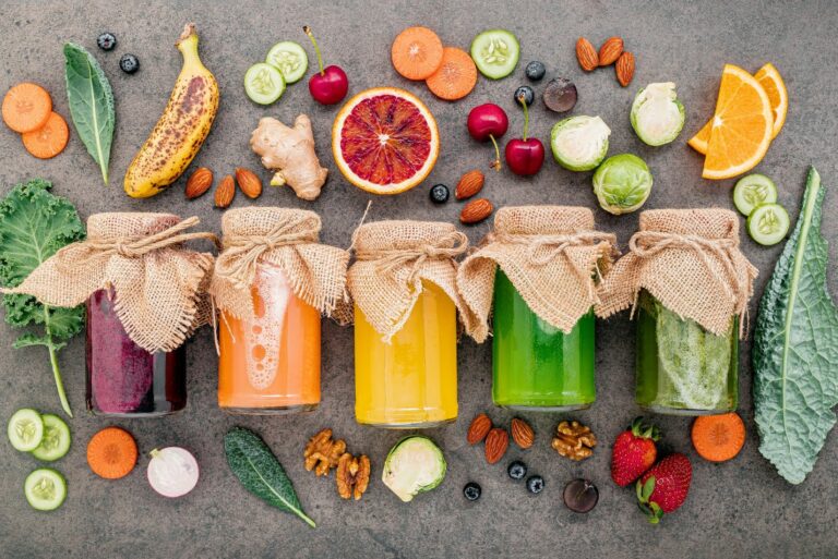 Photo de plusieurs jus de légumes colorés avec des fruits et légumes sur fond gris.