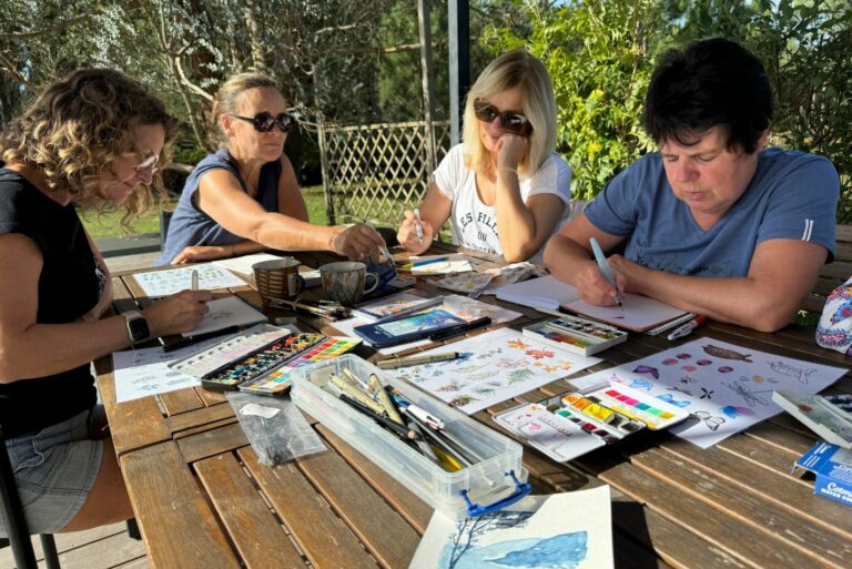 Photo d'un groupe de femmes en train de faire de l'aquarelle sur une table en bois en extérieur.